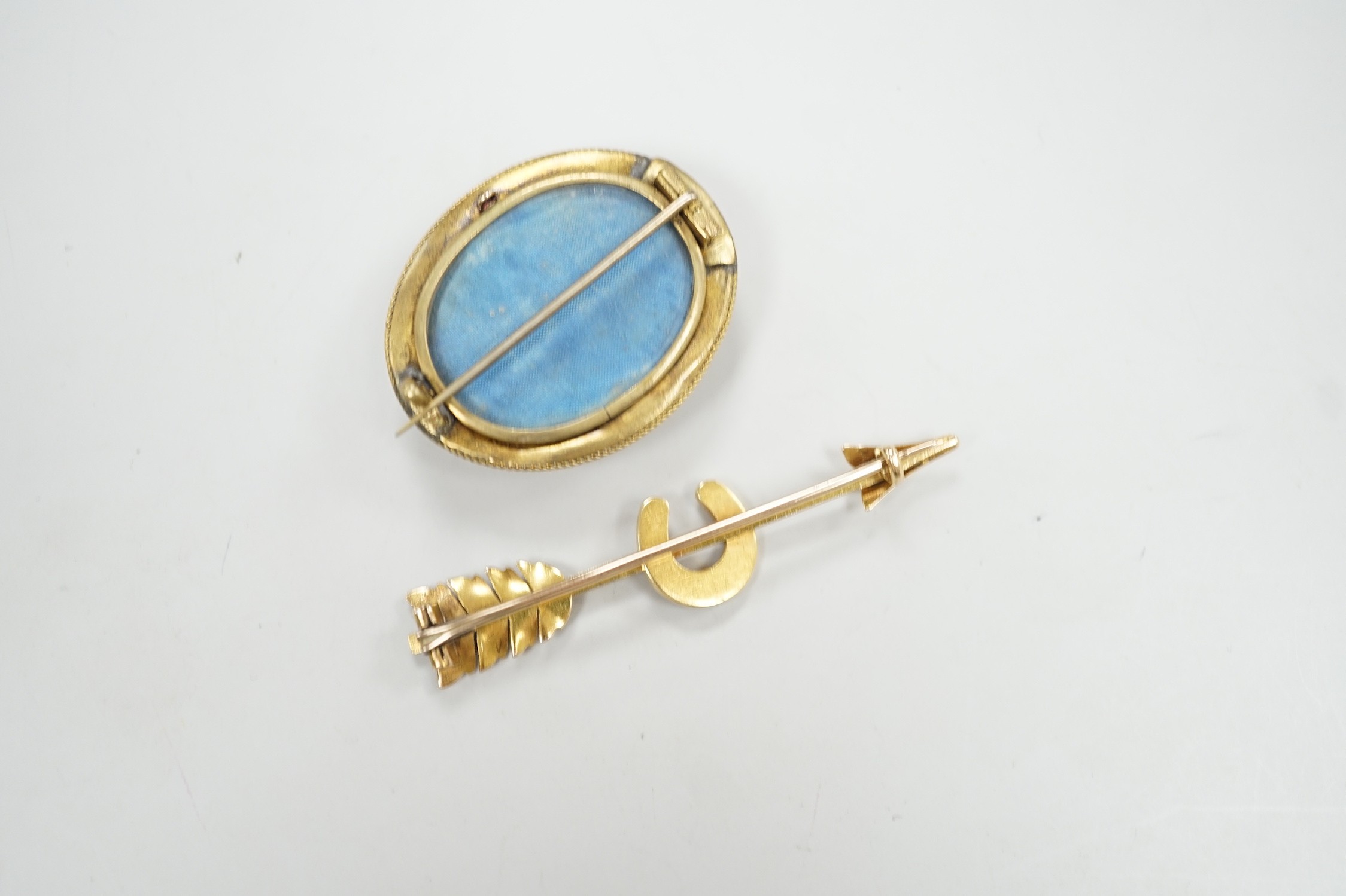 An early 20th century yellow metal, and seed pearl set arrow and horse shoe brooch, 60mm and a Victorian paste set yellow metal oval brooch.